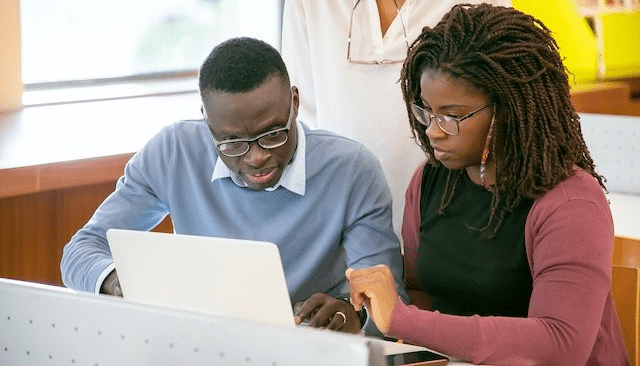 A man and a woman are sitting in front of a laptop